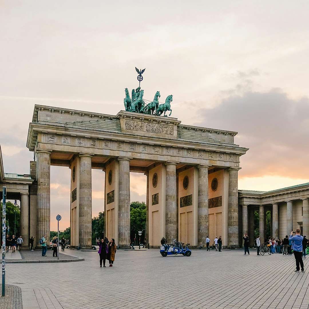 The iconic Brandenburg Gate in Berlin, Germany, captured at sunset with a warm glow. Tourists and locals gather around this historical monument, reflecting Germany's rich cultural heritage. Image used on ASK Consultants' webpage to highlight study abroad opportunities in Germany. ASK Consultants helps students to study in germany.